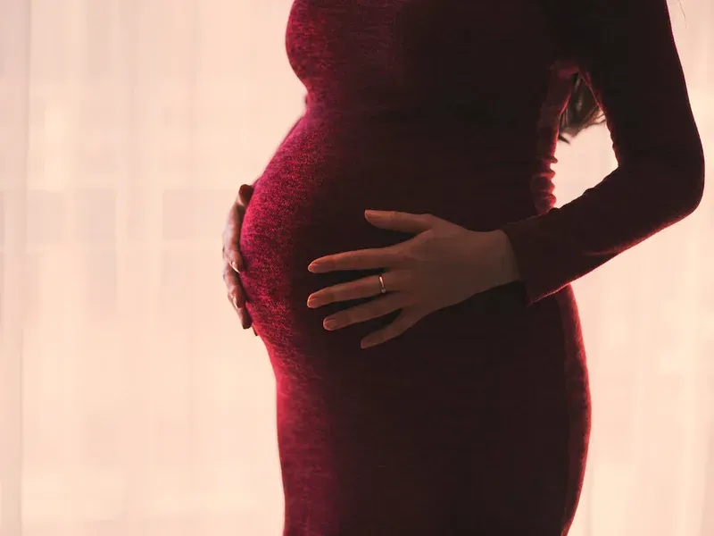 Future maman en robe, la main sur son ventre, devant une fenêtre